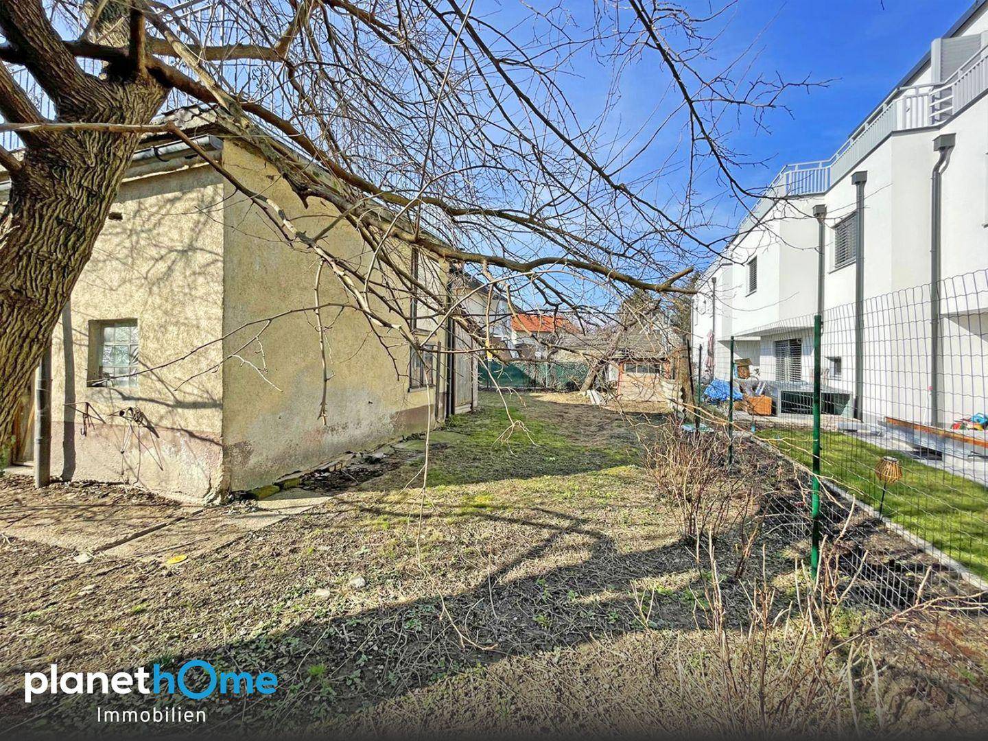 Gartenbereich mit altem Nebengebäude und Blick auf moderne Neubauten in der Nachbarschaft.