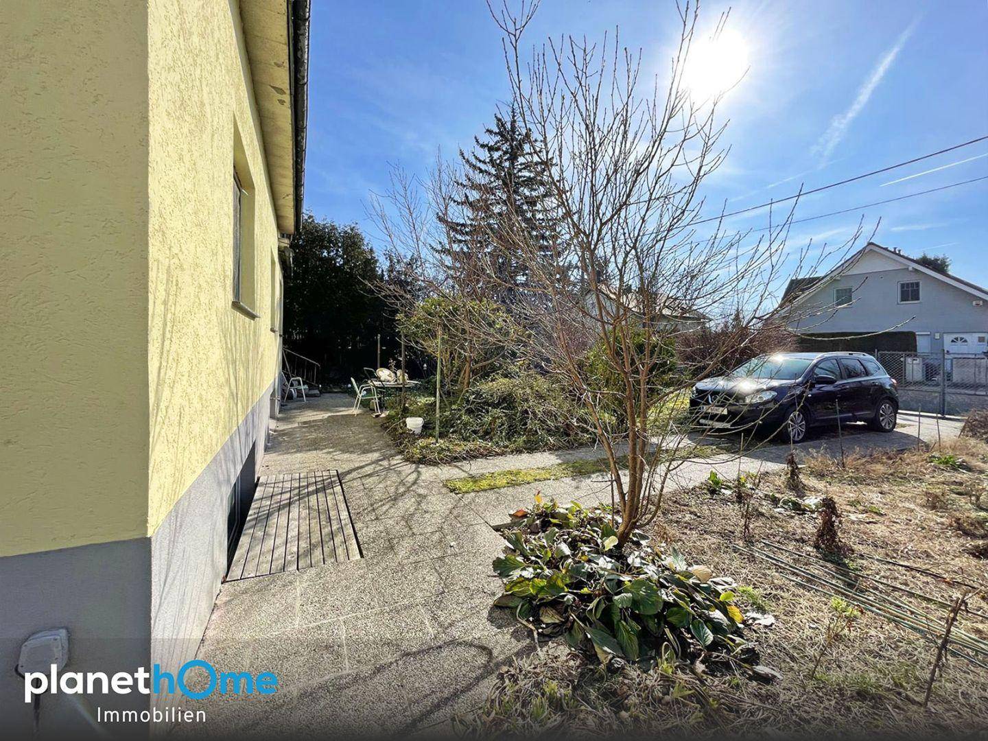 Gepflasterter Weg entlang des Hauses führt zu einem kleinen Sitzbereich im Freien mit Parkplatz im Hintergrund.