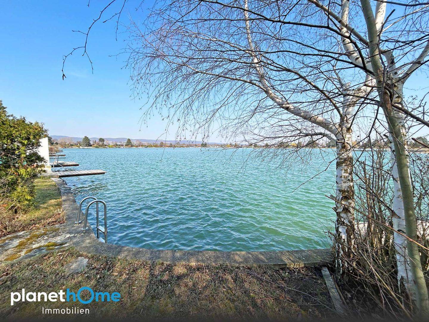 Direkter Zugang zum See mit Steg und Badeleiter, umgeben von natürlicher Vegetation.