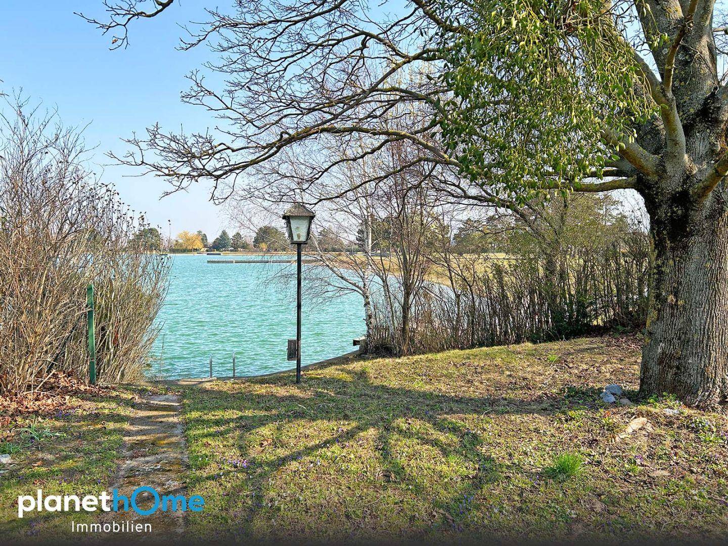 Idyllischer Gartenbereich am Seeufer mit Laterne und Blick auf das ruhige Wasser.