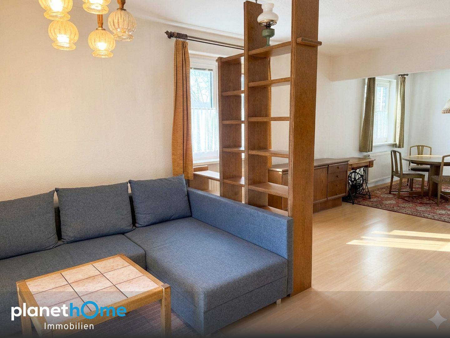 Offener Wohn- und Essbereich mit Sofa, Regal als Raumteiler und Essgruppe im Hintergrund.