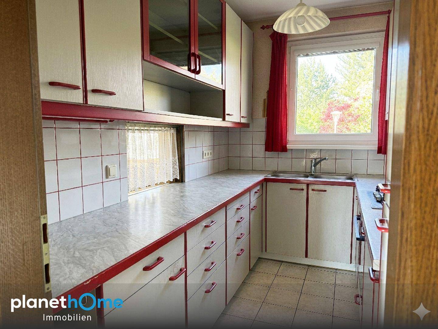 Küche im Landhausstil mit roten Akzenten, weißen Schränken und Fenster über der Spüle.