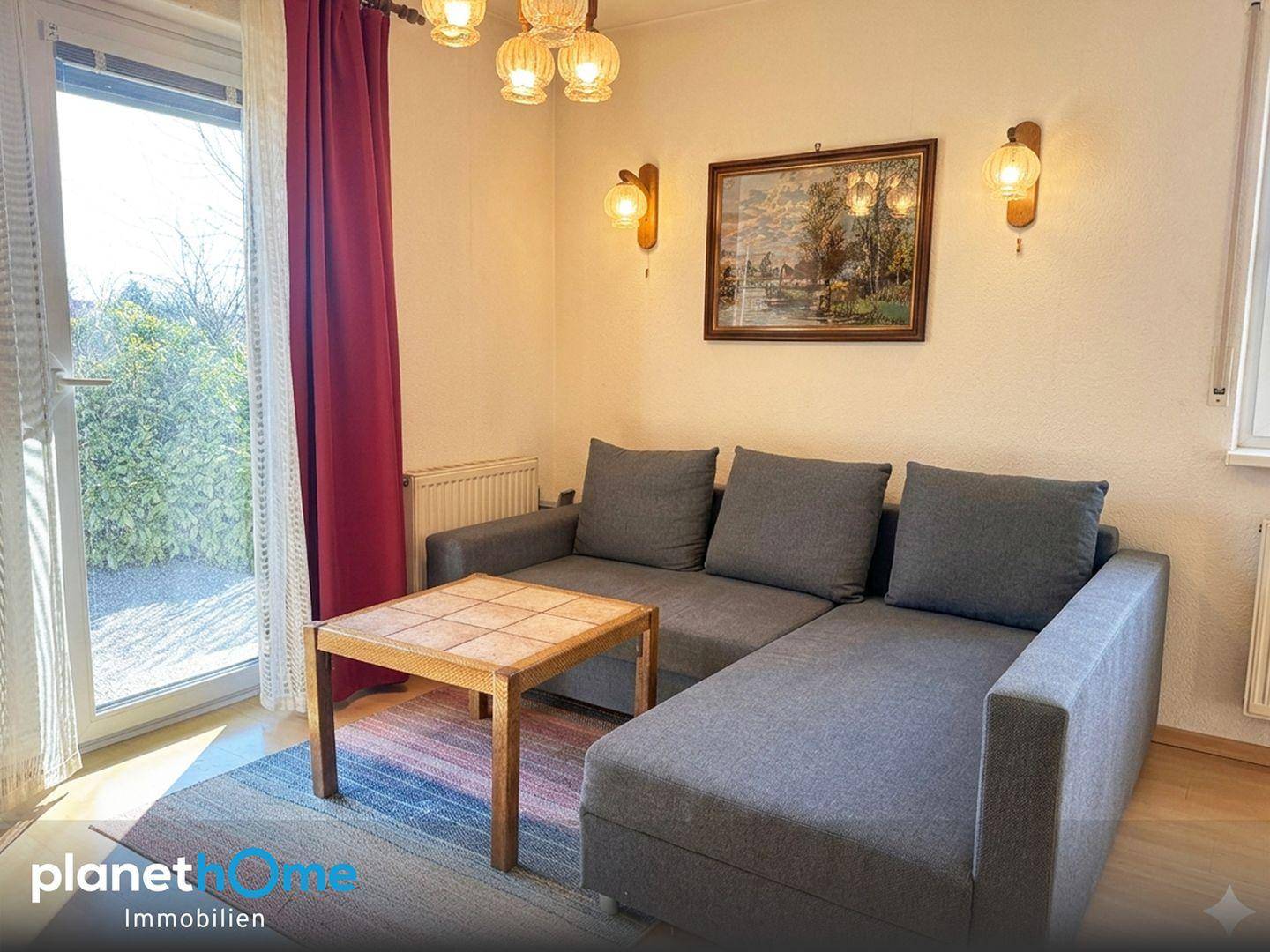 Wohnzimmer mit bequemer Couch, Teppich und Zugang zu einem sonnigen Außenbereich.