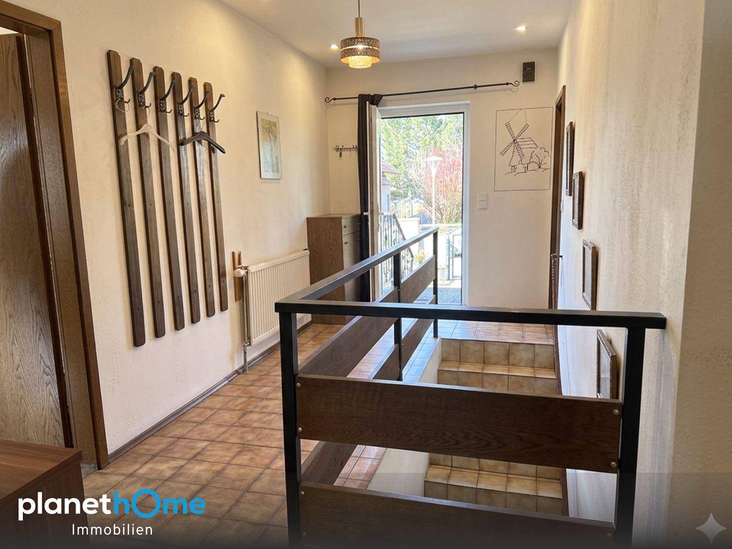 Heller Eingangsbereich mit Treppe, Garderobe und Blick ins Grüne durch die Haustür.