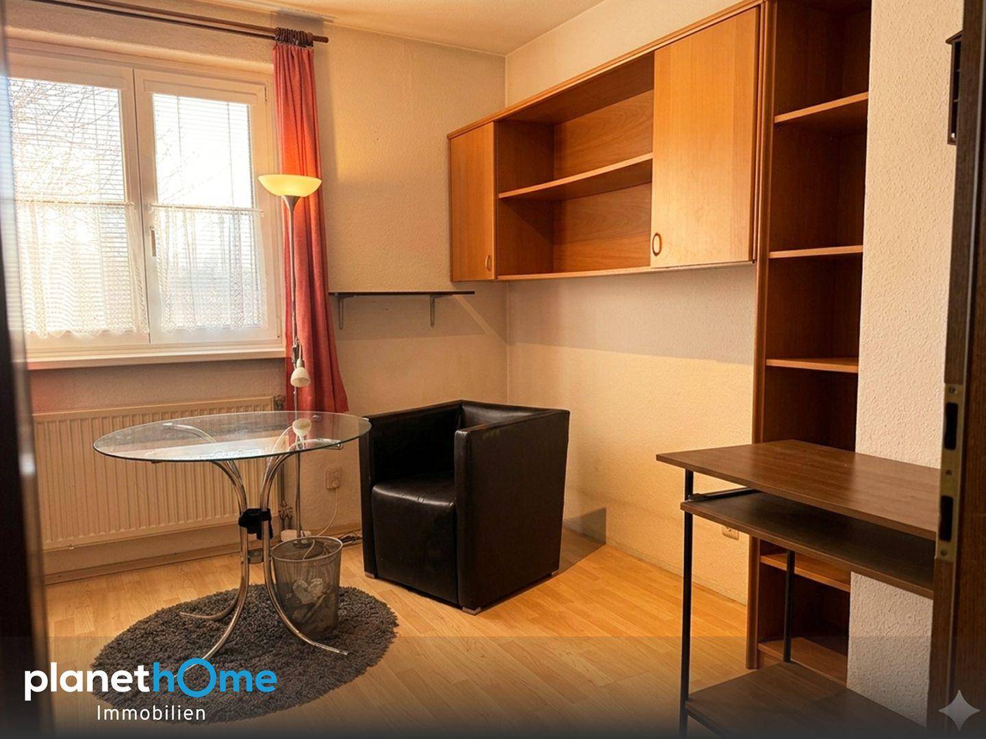 Helles Zimmer mit Glastisch, Sessel und Regalen, ideal als Büro oder Gästezimmer.
