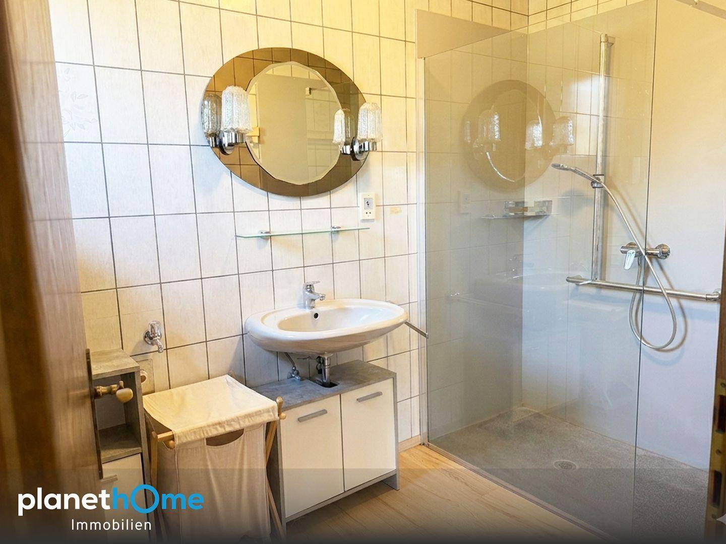 Modernisiertes Badezimmer mit ebenerdiger Dusche, Waschtisch und großem Spiegel.