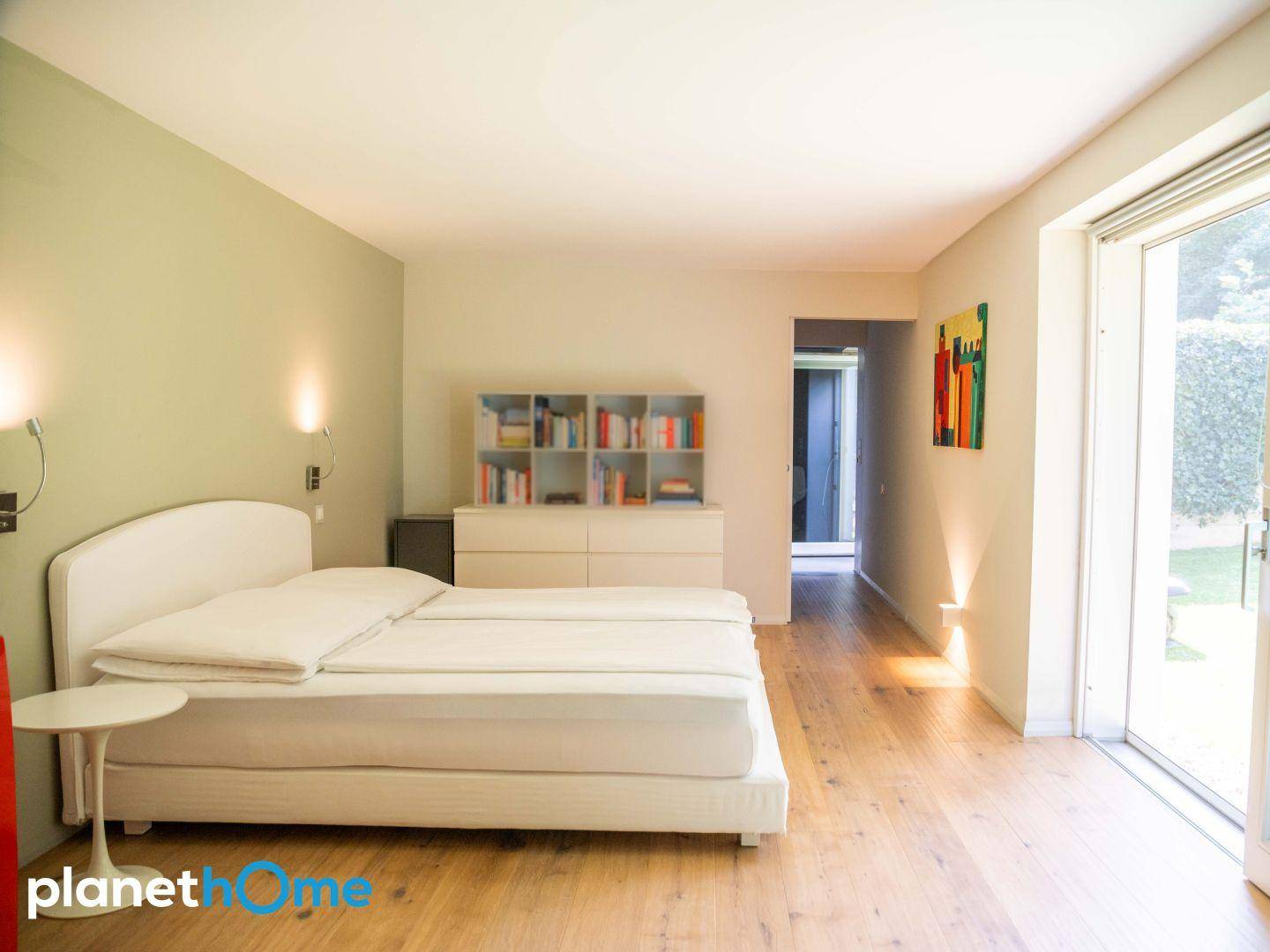 Geräumiges Schlafzimmer mit Holzboden, Bücherregal und Zugang zum Außenbereich.