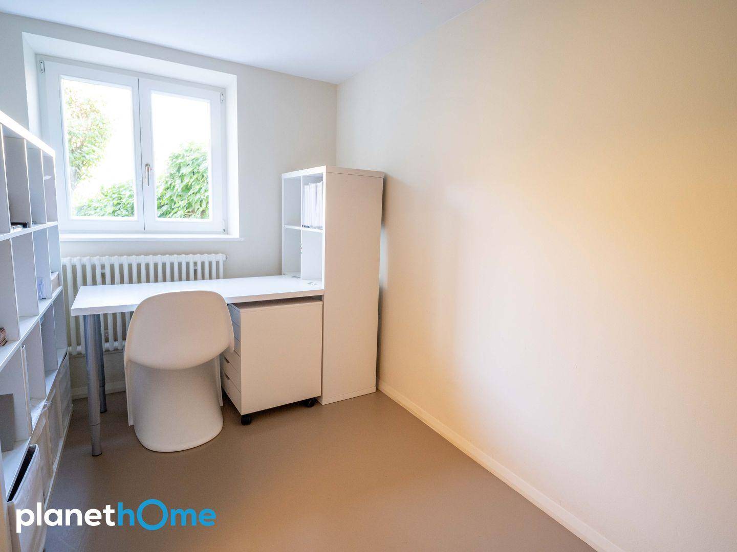 Helles Arbeitszimmer mit Schreibtisch, Regalen und Fensterblick ins Grüne.