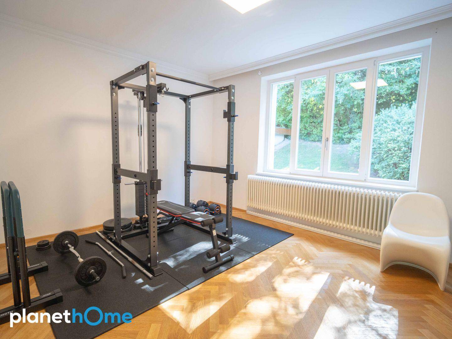 Privater Fitnessraum mit Trainingsgeräten, Parkettboden und Blick ins Grüne.