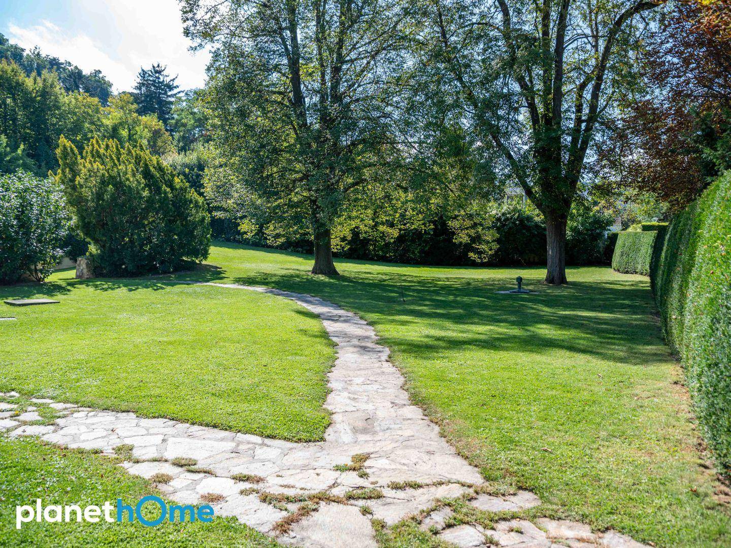 Idyllischer Gartenweg aus Natursteinplatten, umgeben von Rasen und Hecken.