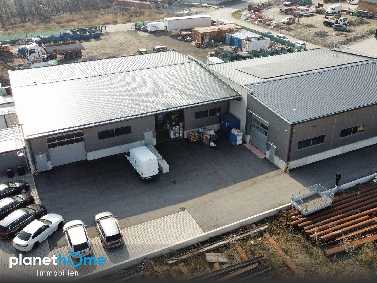 Luftaufnahme eines Gewerbekomplexes mit mehreren Hallen, Parkplätzen und angrenzendem Industriegelände.