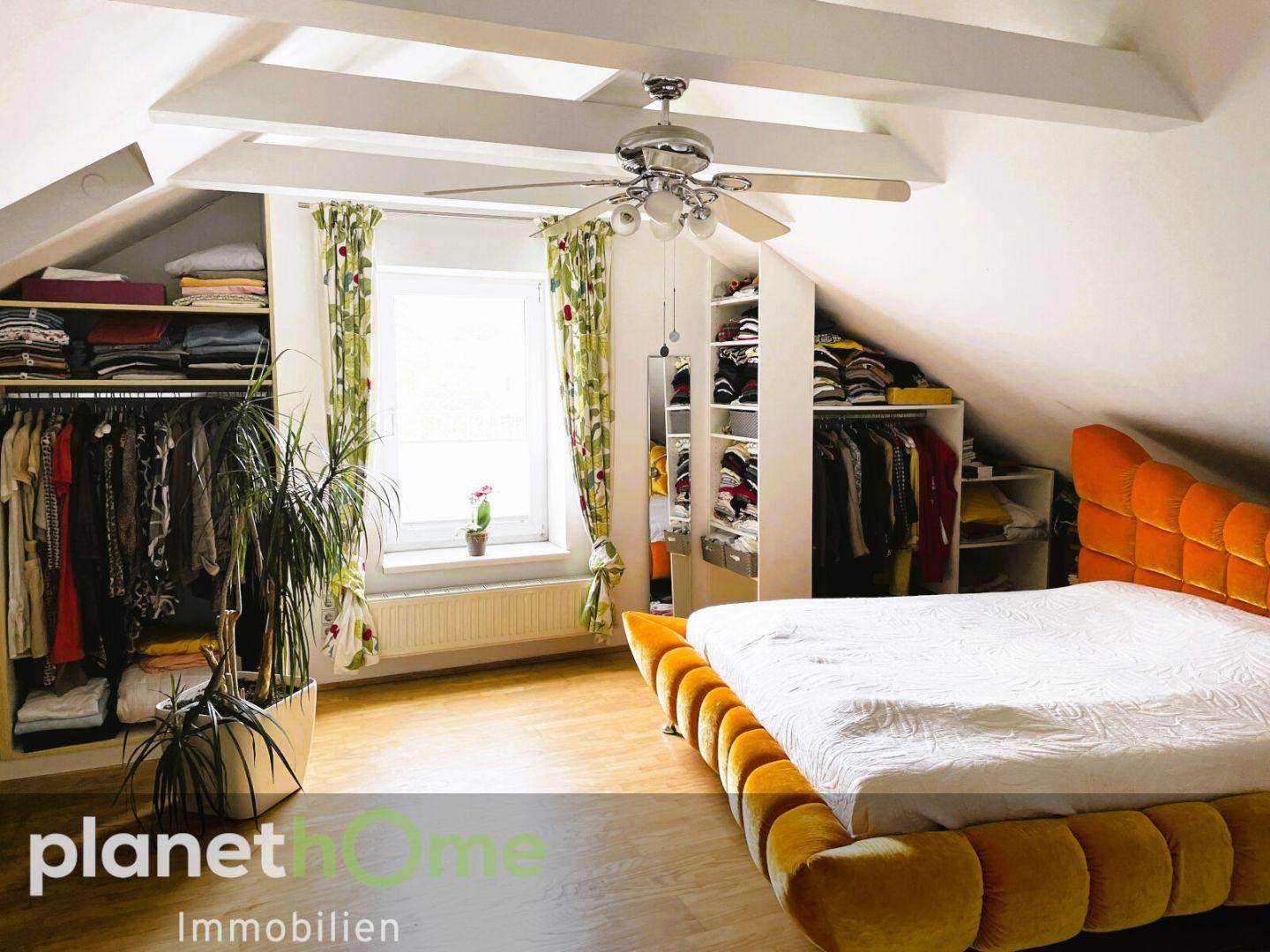 Schlafzimmer im Dachgeschoss mit Dachschrägen, offenem Kleiderschrank und Deckenventilator.