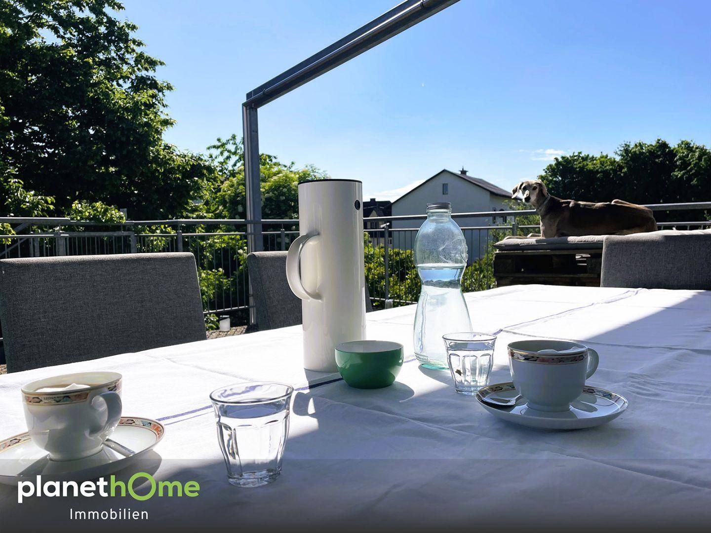 Gemütlicher Frühstückstisch auf der Terrasse mit Blick ins Grüne an einem sonnigen Tag.