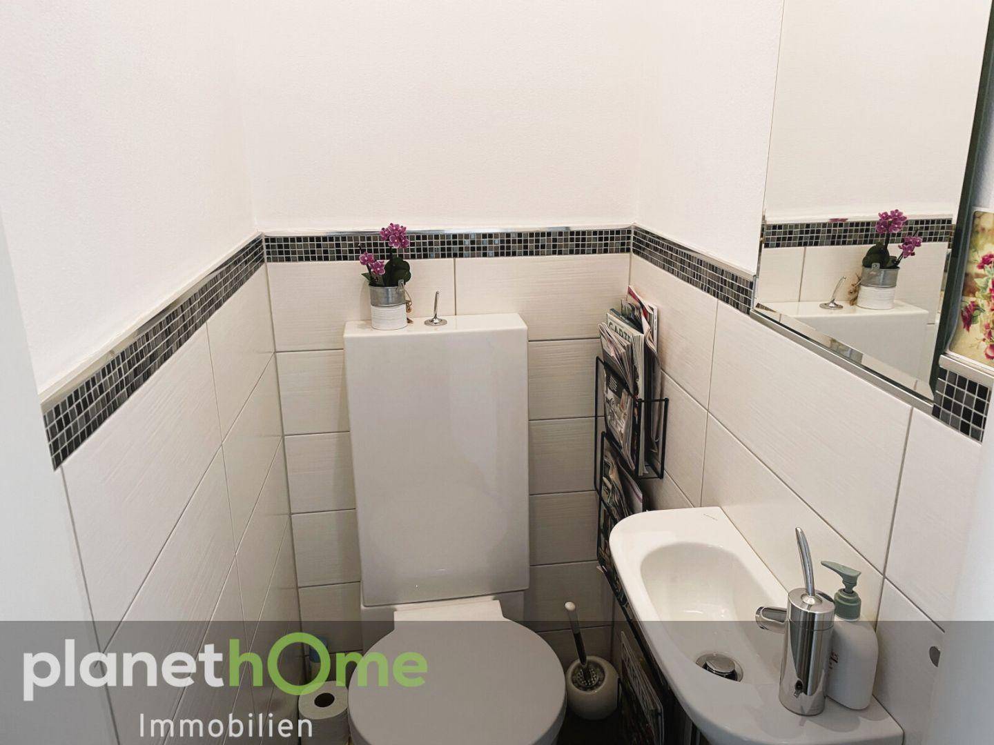 Kleines Gäste-WC mit WC, Waschbecken und dekorativen Fliesenbordüren.