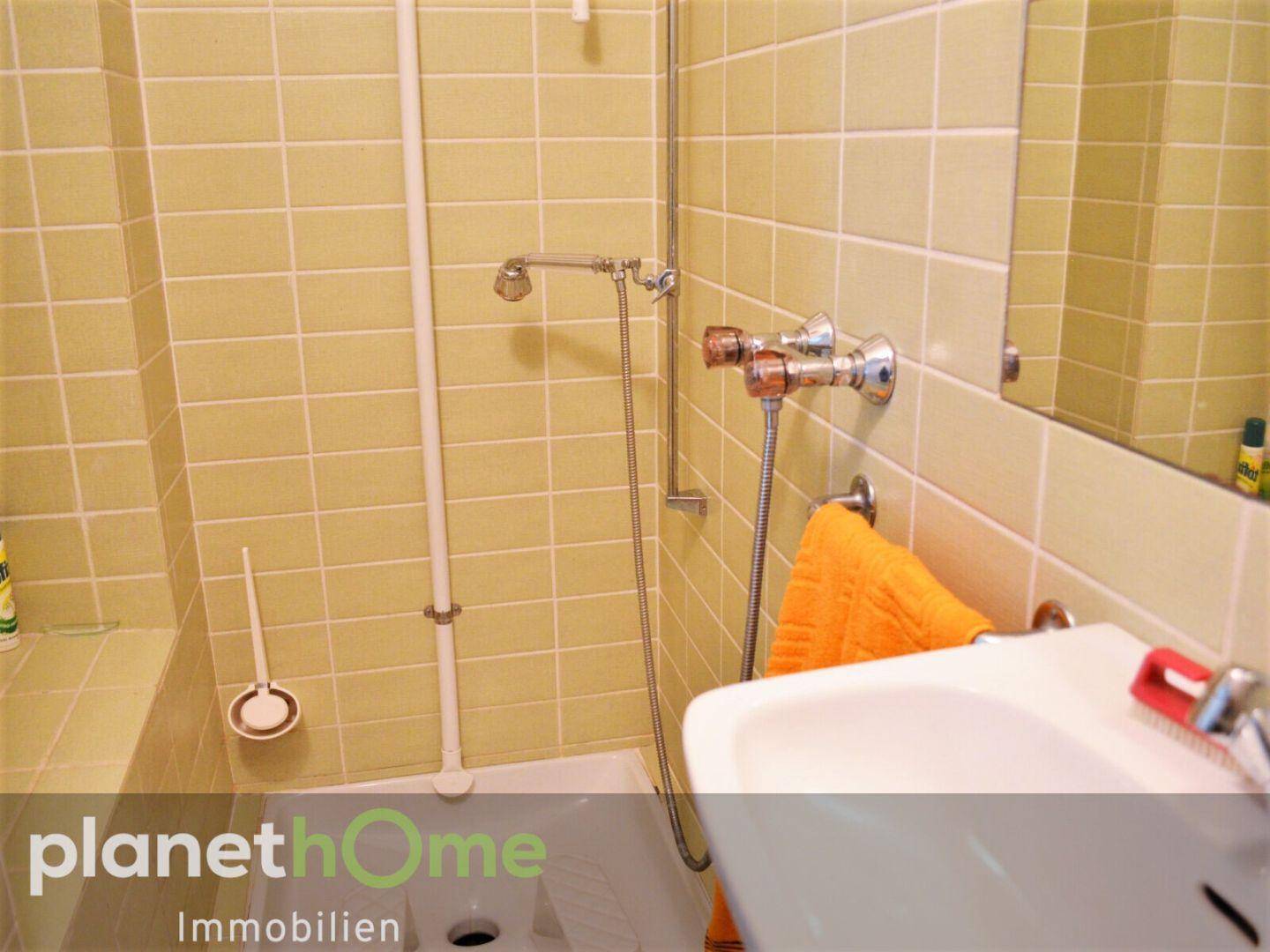 Badezimmer mit gelben Fliesen, Dusche und Waschbecken im 80er-Jahre-Stil.