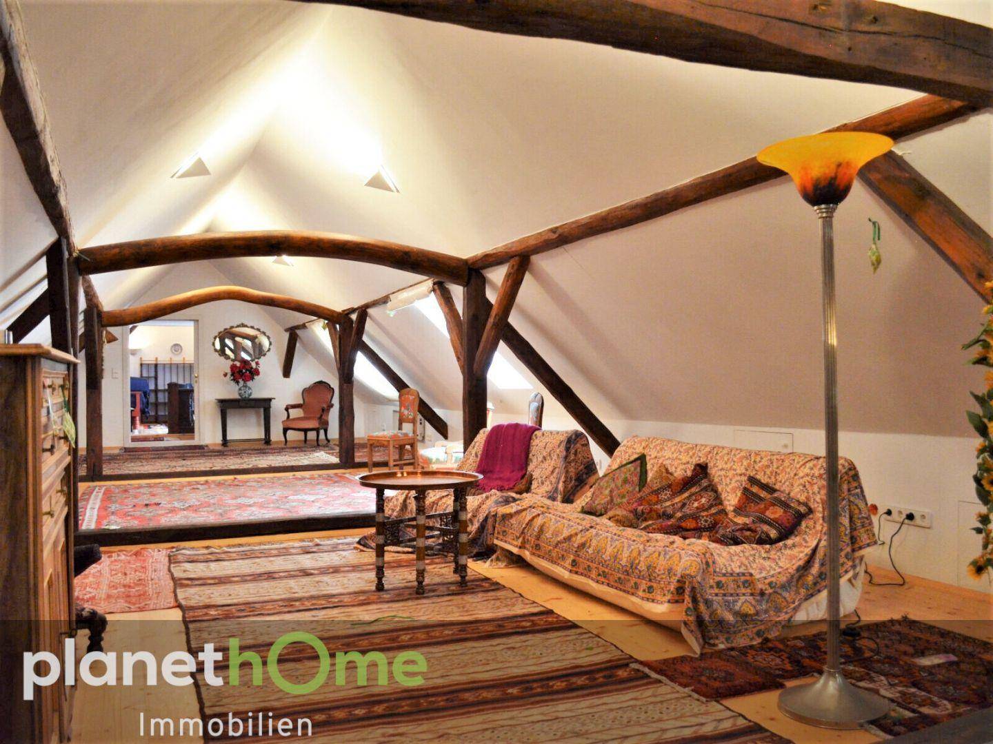 Weitläufiges Dachgeschoss mit Holzbalken, Teppichen und Blick in den hinteren Bereich.
