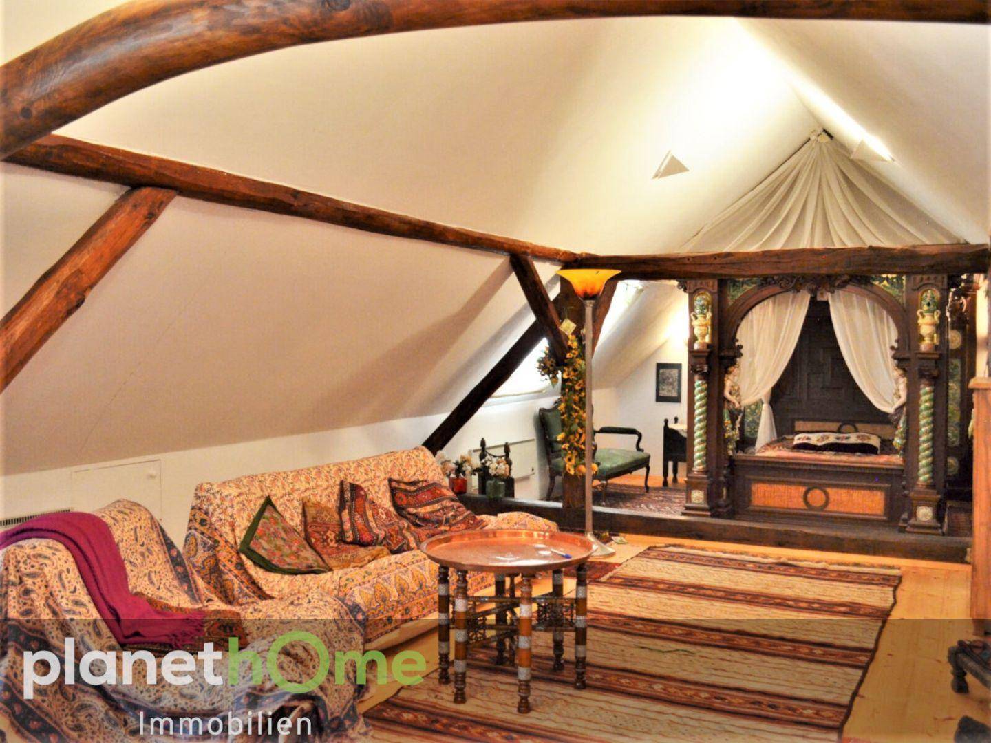Geräumiges Dachgeschoss mit Holzbalken, gemütlicher Sitzecke und Himmelbett.