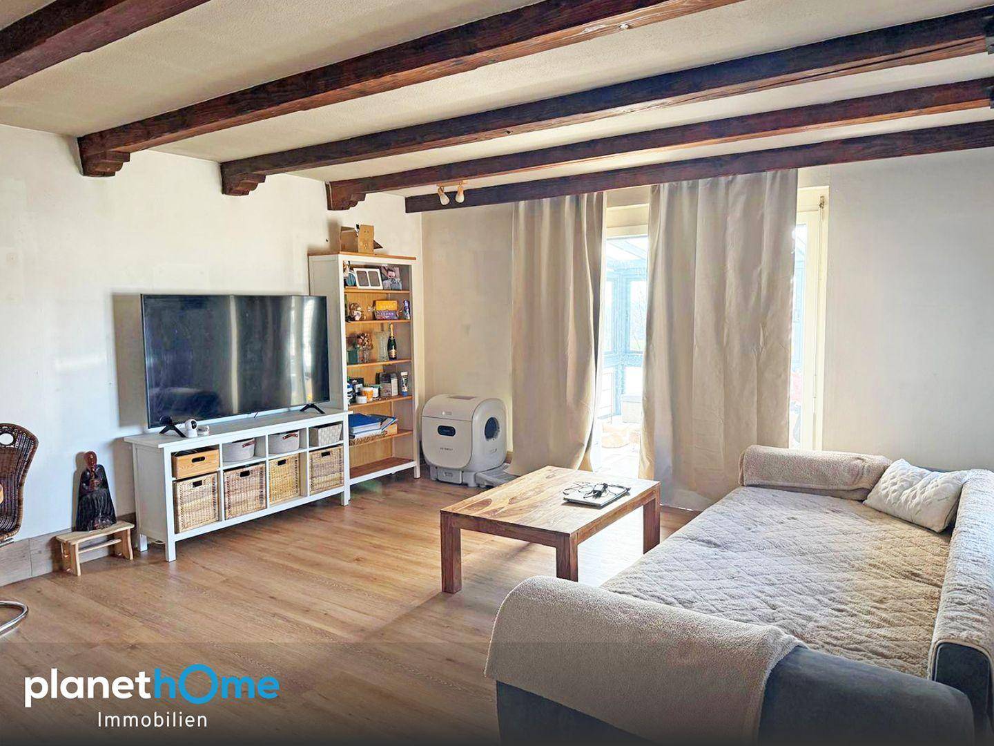 Gemütliches Wohnzimmer mit sichtbaren Holzbalken, Parkettboden und Zugang zum Außenbereich.
