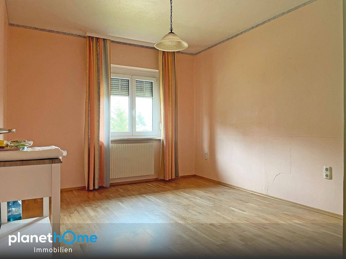 Helles Zimmer mit Parkettboden, Fenster und pastellfarbenen Wänden.
