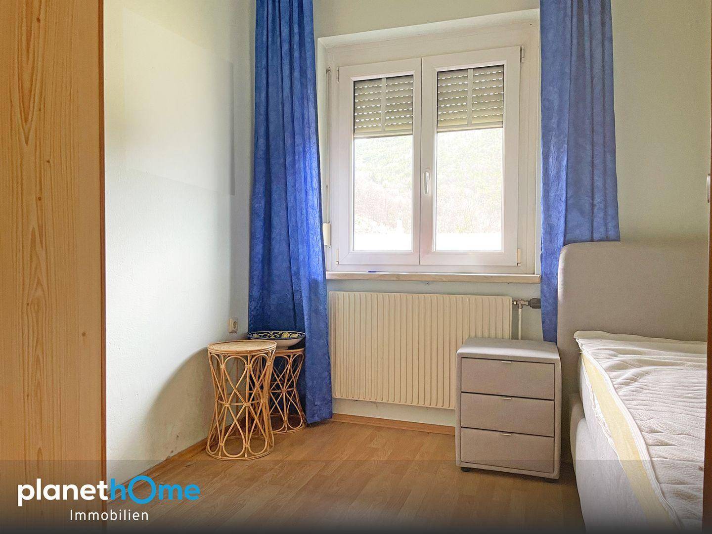 Schlafzimmer mit Holzboden, Fenster und blauen Vorhängen.