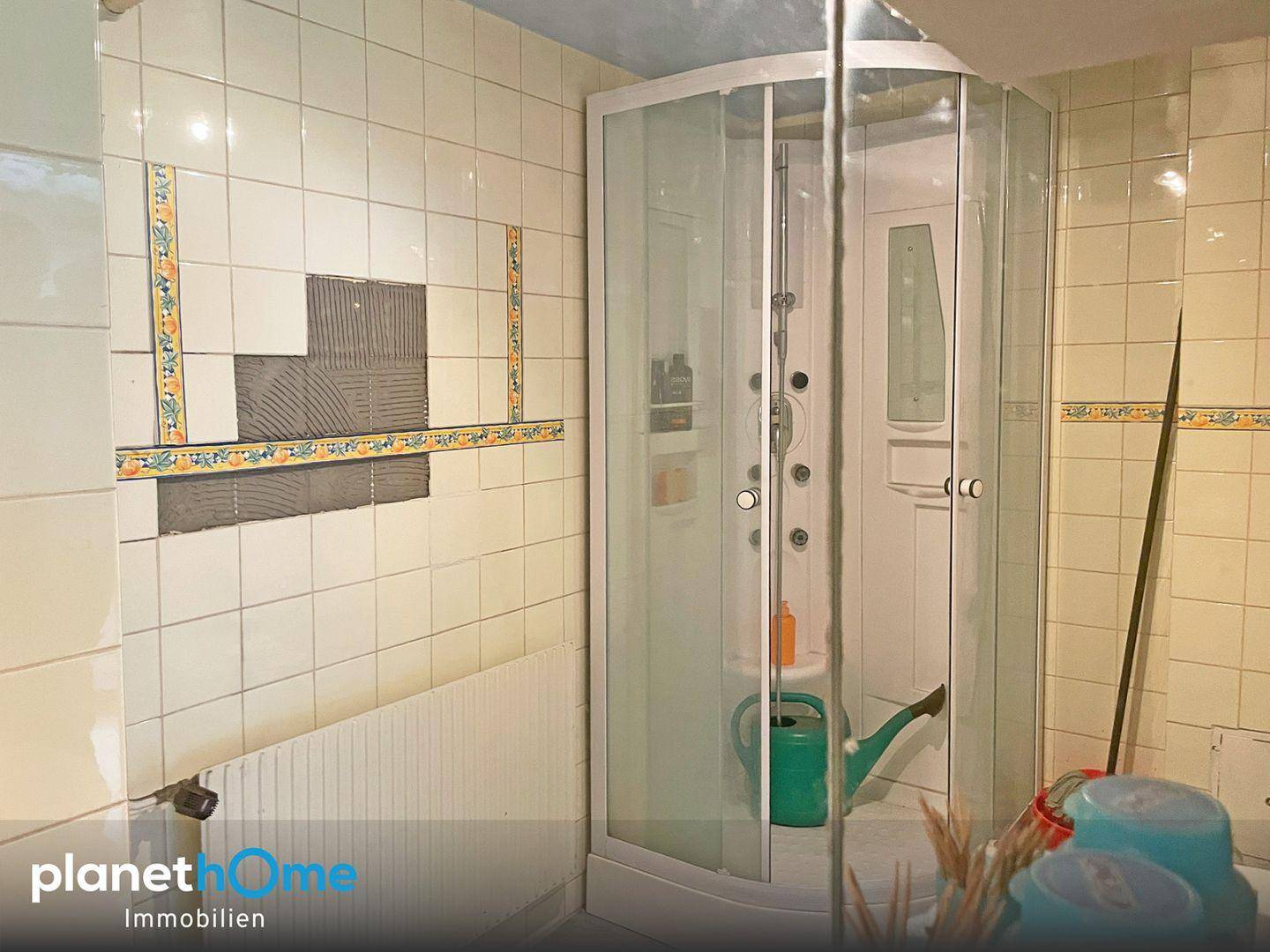 Badezimmer mit Duschkabine und älteren Fliesen.