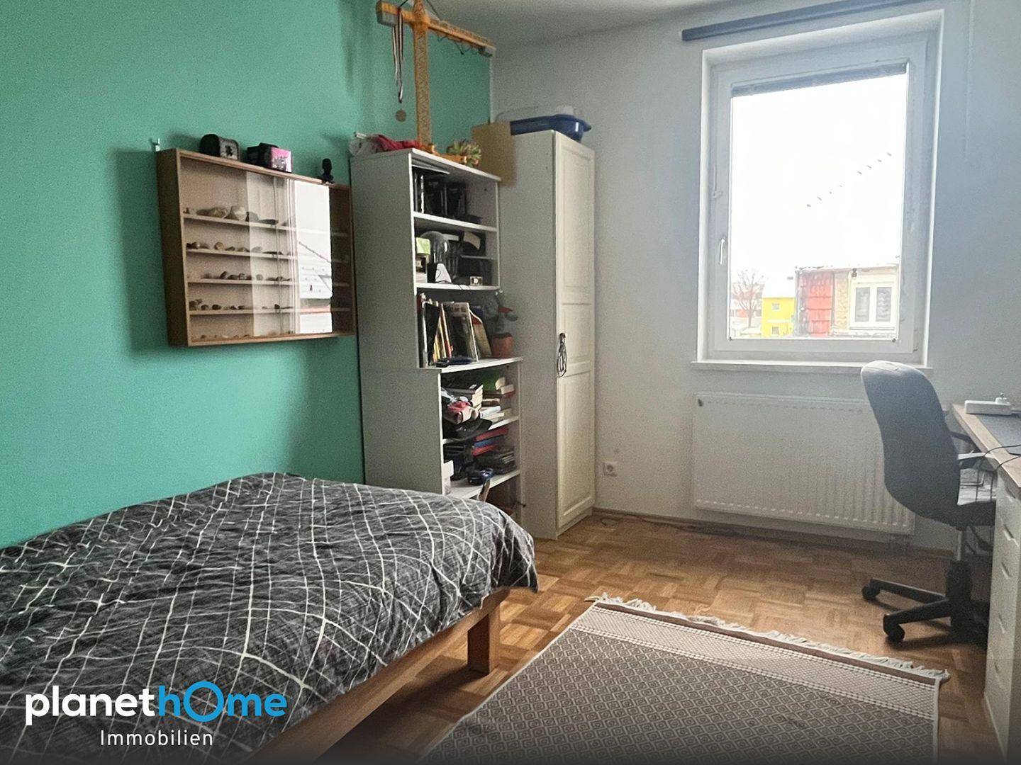 Schlafzimmer mit Einzelbett, Schreibtisch und einer farbigen Wand in Türkis.