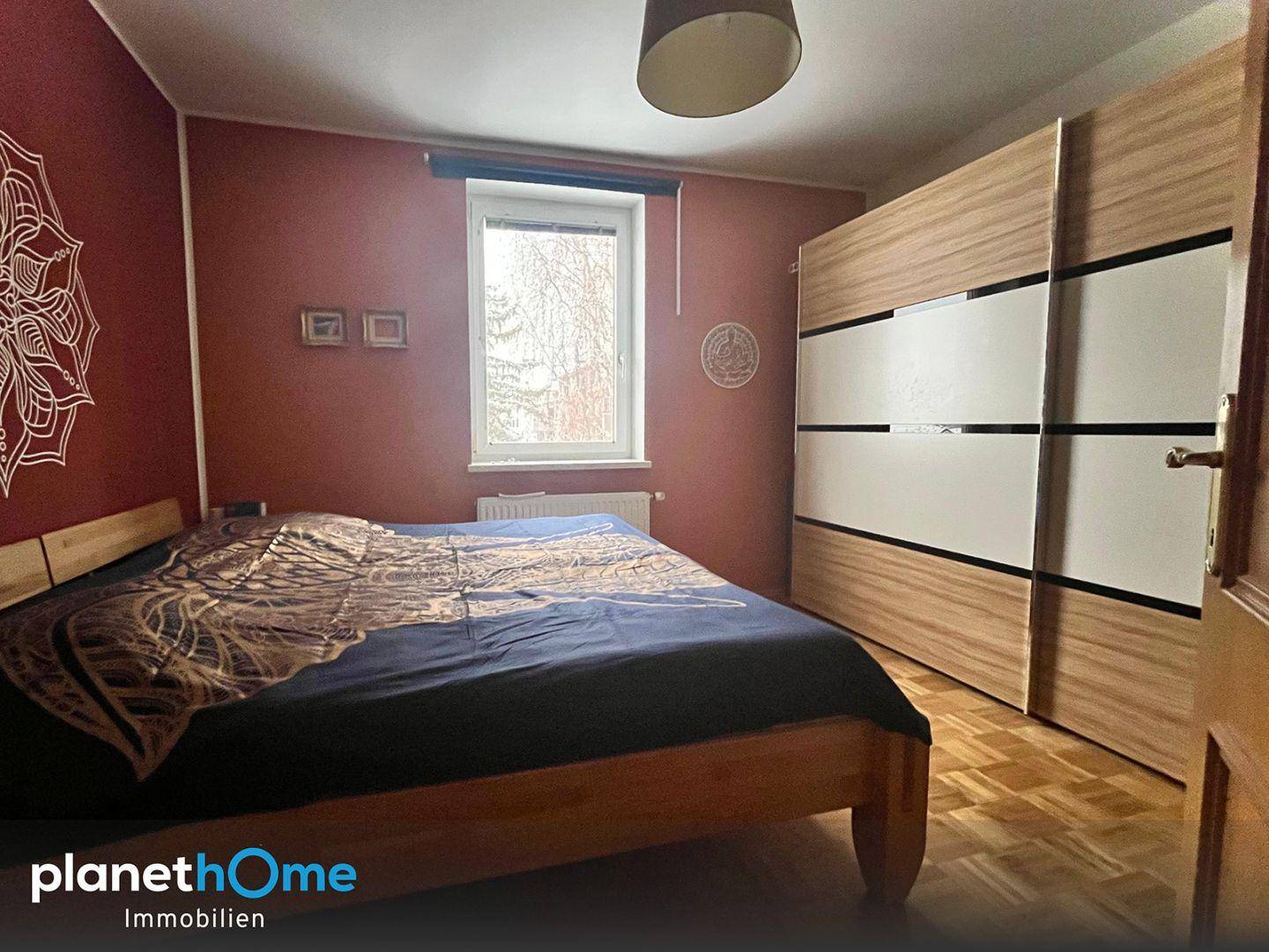 Schlafzimmer mit Doppelbett und großem Schiebetürenschrank vor einer roten Wand.