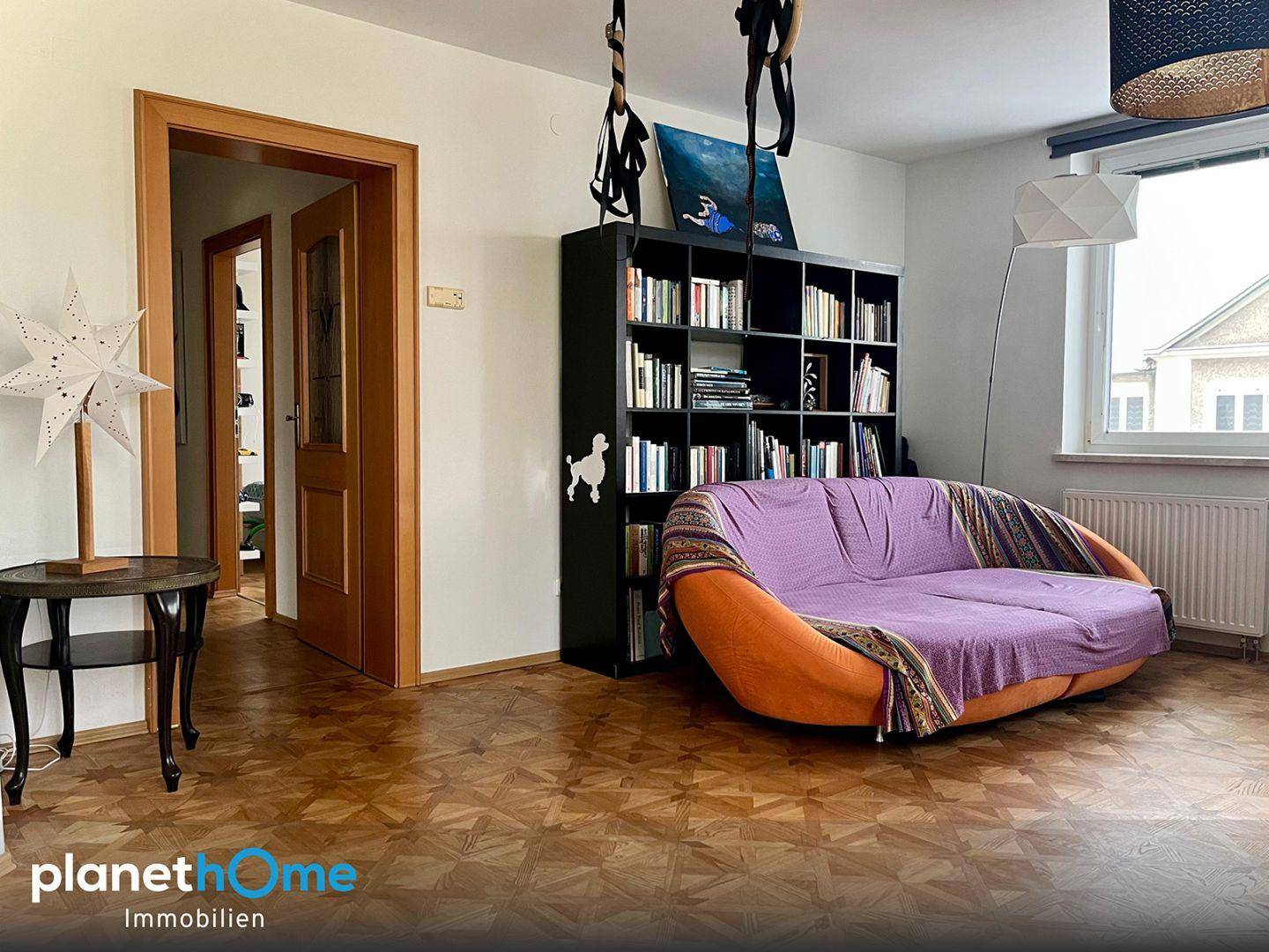 Gemütlicher Raum mit Sofa, Bücherregal und dekorativem Parkettboden.