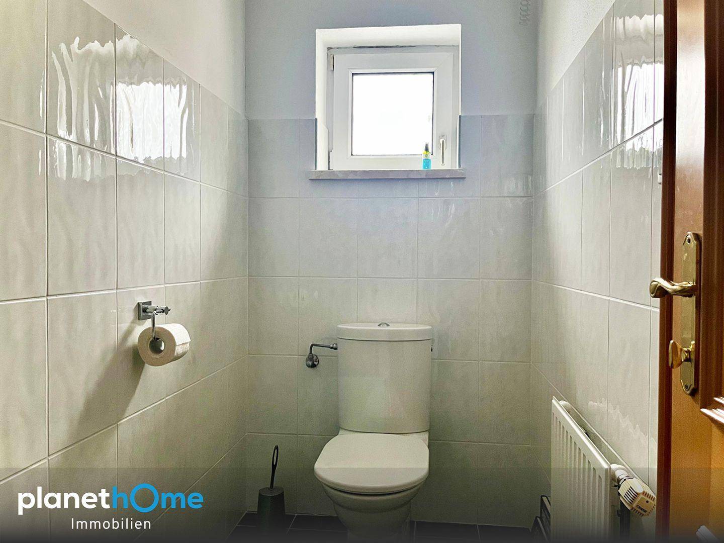 Kleines WC mit Toilette und Fenster, komplett gefliest in hellem Weiß.