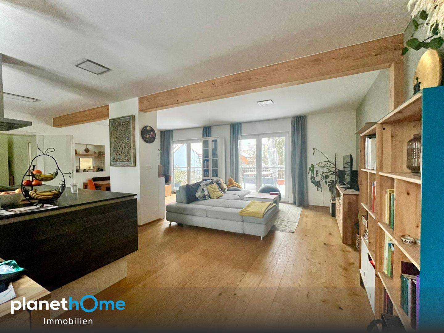 Helles Wohnzimmer mit bequemer Couch, Bücherregal und Zugang zu einem Balkon.
