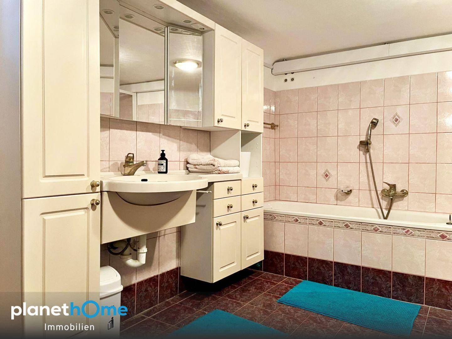 Badezimmer im Untergeschoss mit Waschbecken, Badewanne und rosa-braunen Fliesen.