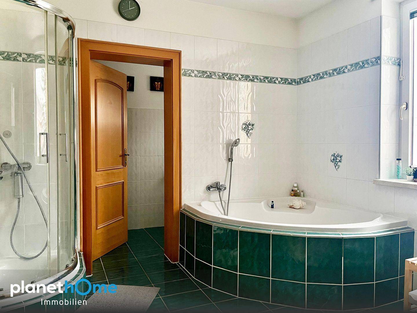 Badezimmer mit Eckbadewanne und separater Duschkabine in grünen Fliesen.
