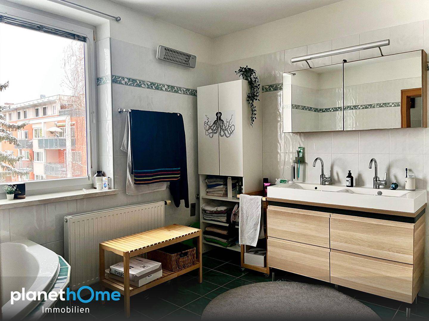 Helles Badezimmer mit Doppelwaschbecken, Spiegelschrank und Fenster.