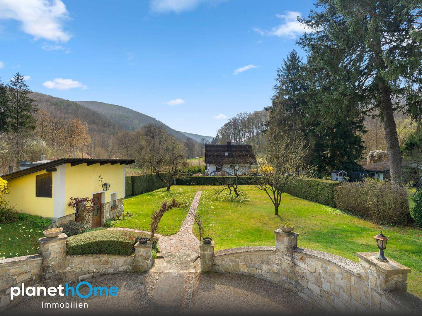 Gepflasterte Terrasse mit Steinmauer und weitem Blick über den grünen Garten und die Hügel.