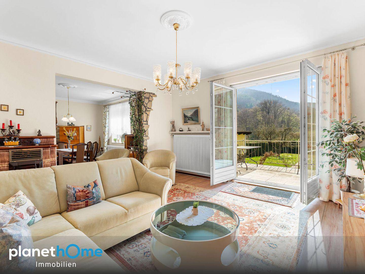 Helles Wohnzimmer mit Sofa, Teppich und Zugang zu einem Balkon mit Bergblick.