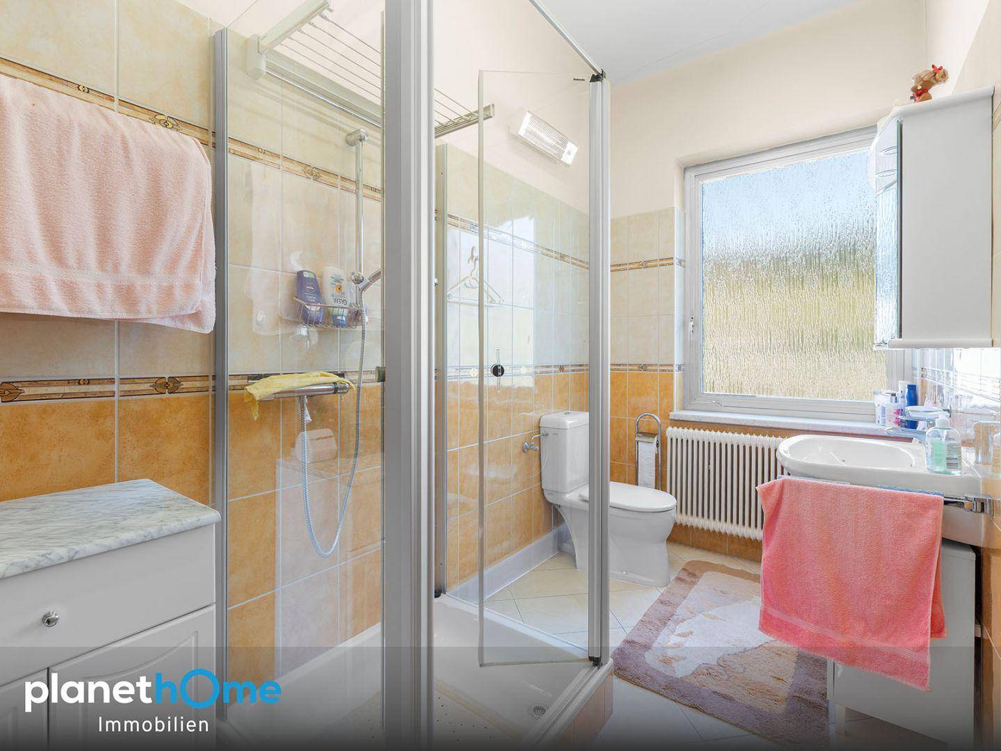 Badezimmer mit Dusche, WC und Fenster, ausgestattet mit funktionalen Fliesen.