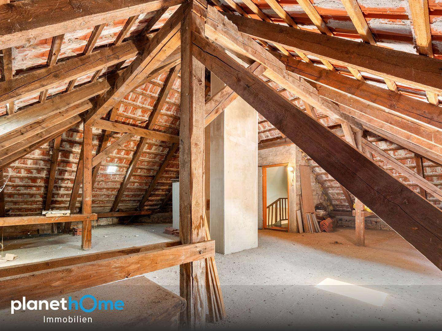 Unausgebauter Dachboden mit sichtbaren Holzbalken und Ziegeln, bietet Ausbaupotenzial.