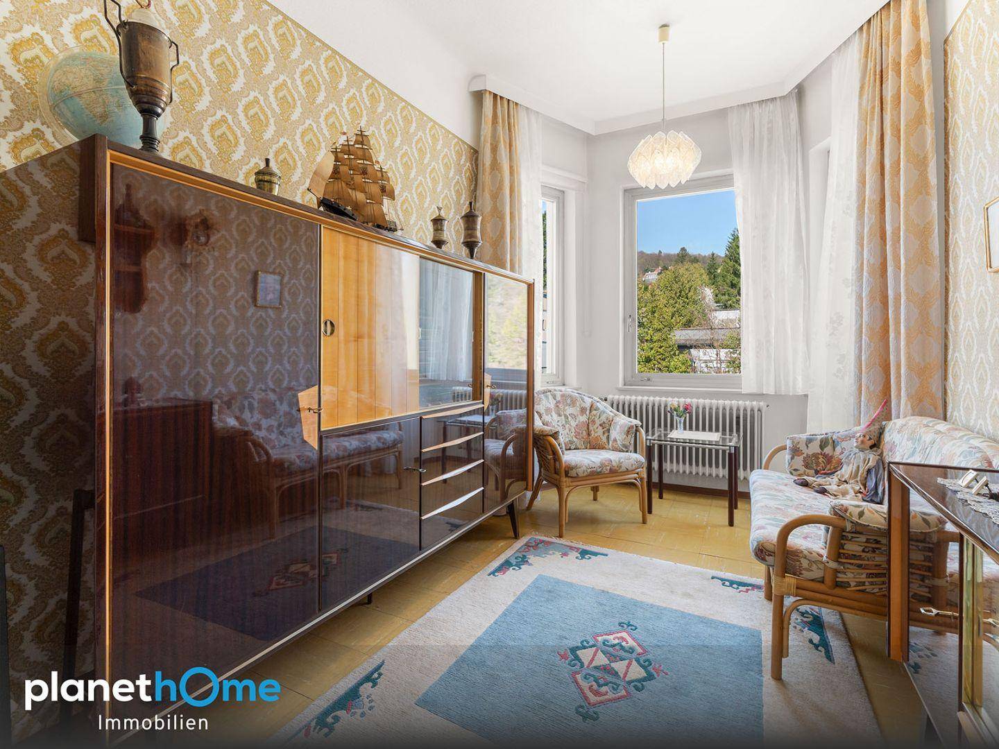 Helles Zimmer mit Vintage-Möbeln, Teppich und Fenster mit Blick auf die Umgebung.