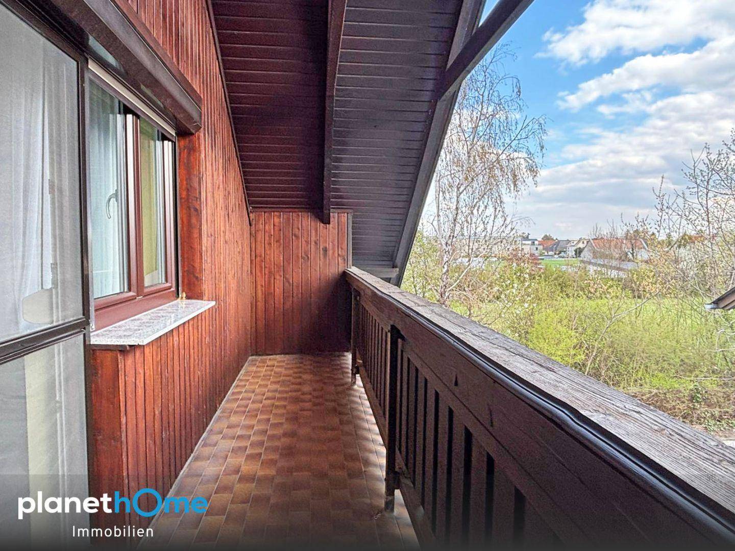 Überdachter Balkon mit Holzverkleidung und Blick ins Grüne.