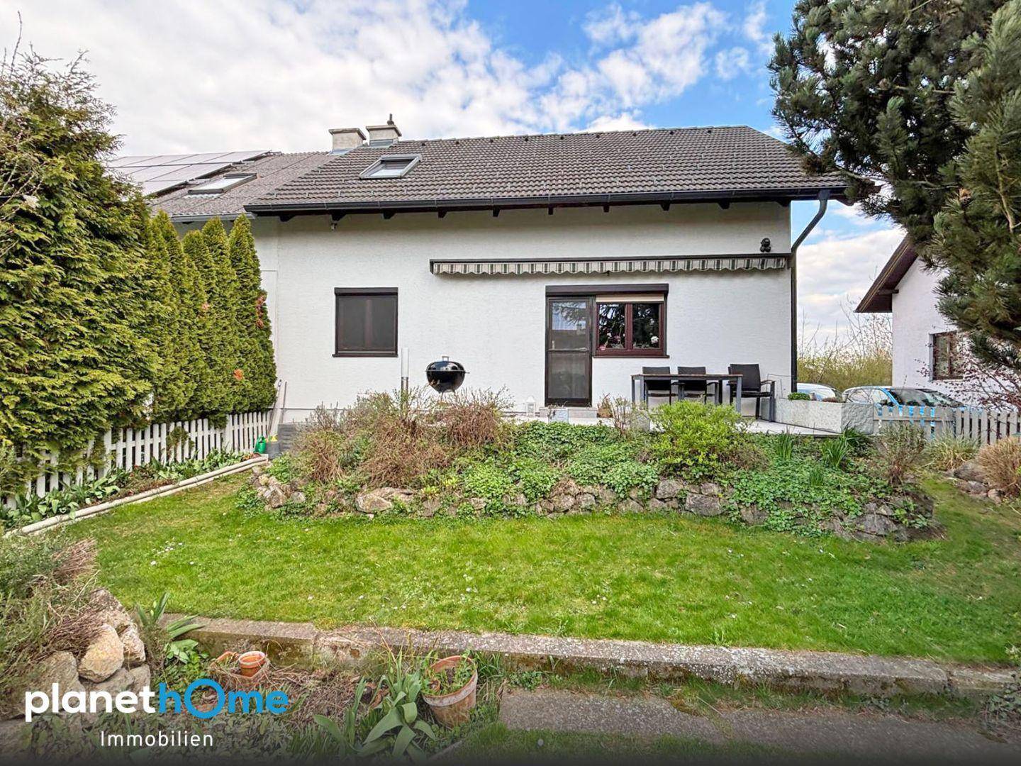 Rückansicht des Hauses mit Terrasse, Garten und Photovoltaikanlage auf dem Dach.