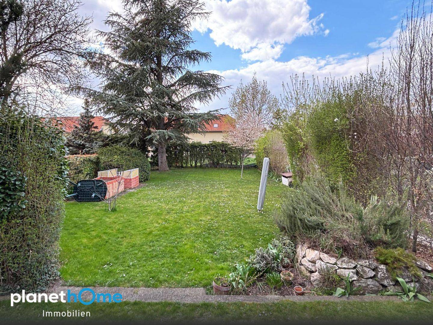 Weitläufiger Garten mit Rasenfläche, Bäumen und Sträuchern unter blauem Himmel.