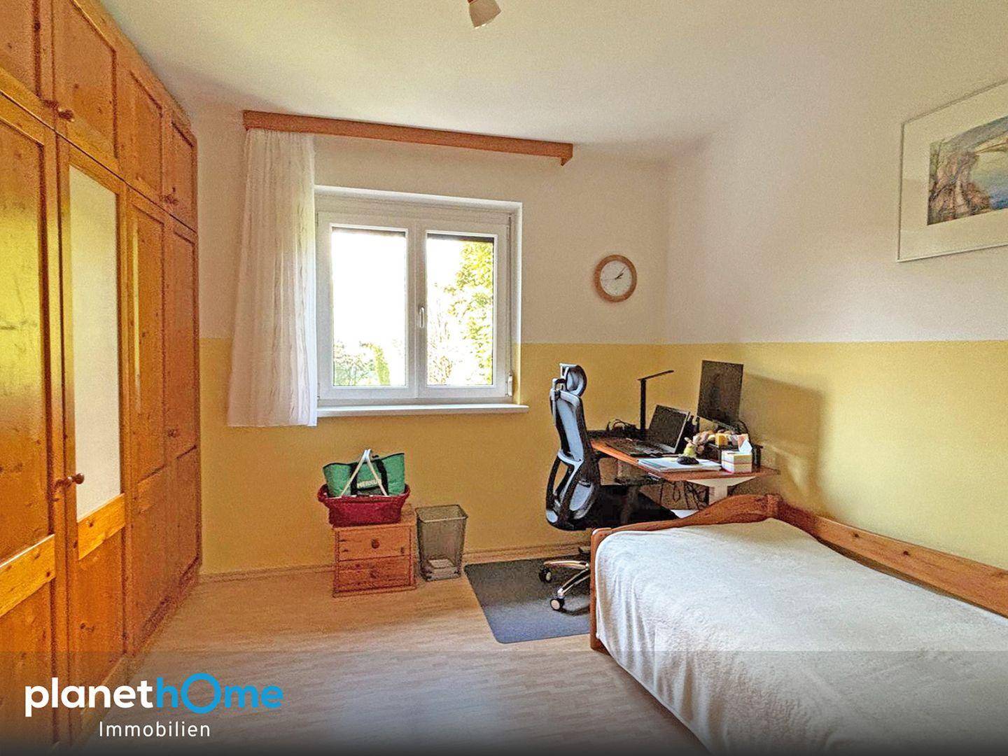 Helles Zimmer mit Einzelbett, Schreibtisch und großem Holzschrank.