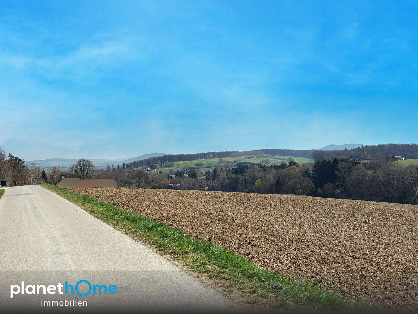 Landstraße neben einem Acker mit weitem Blick auf die hügelige Landschaft.