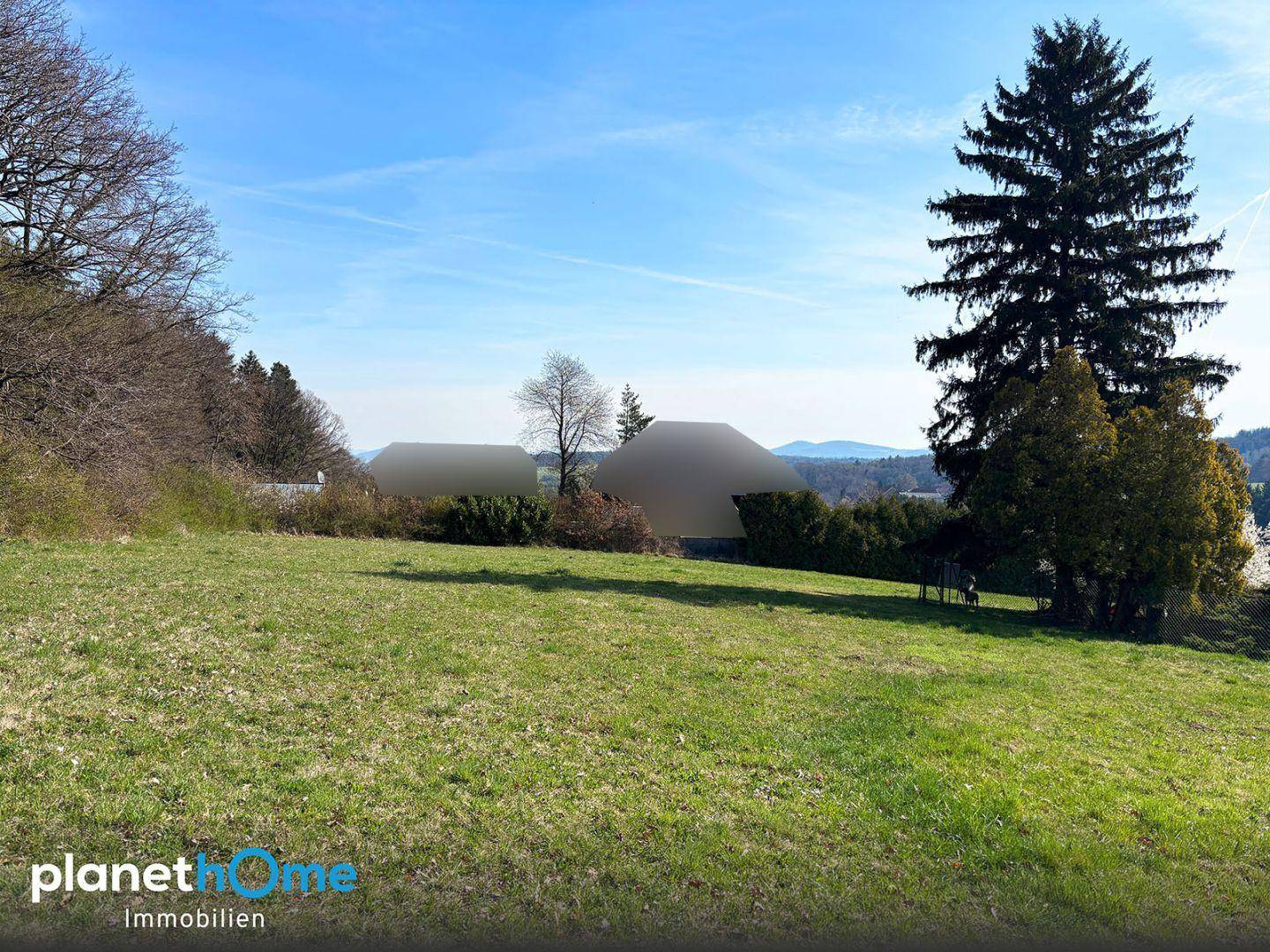 Weitläufige Wiese mit Fernblick auf bewaldete Hügel und einzelne Bäume.