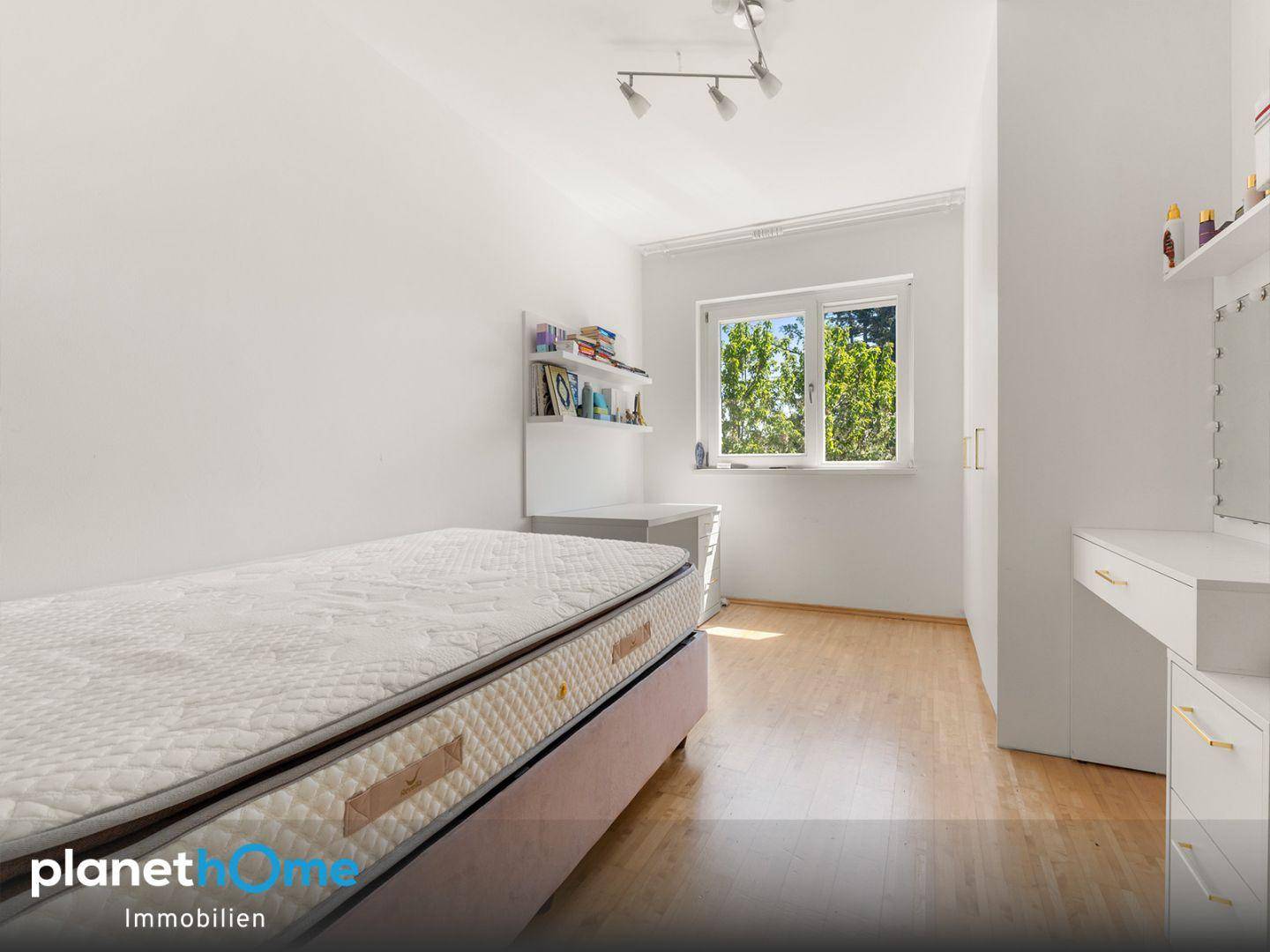 Schlafzimmer mit Holzboden, Einzelbett und einem Fenster, das viel Tageslicht hereinlässt.