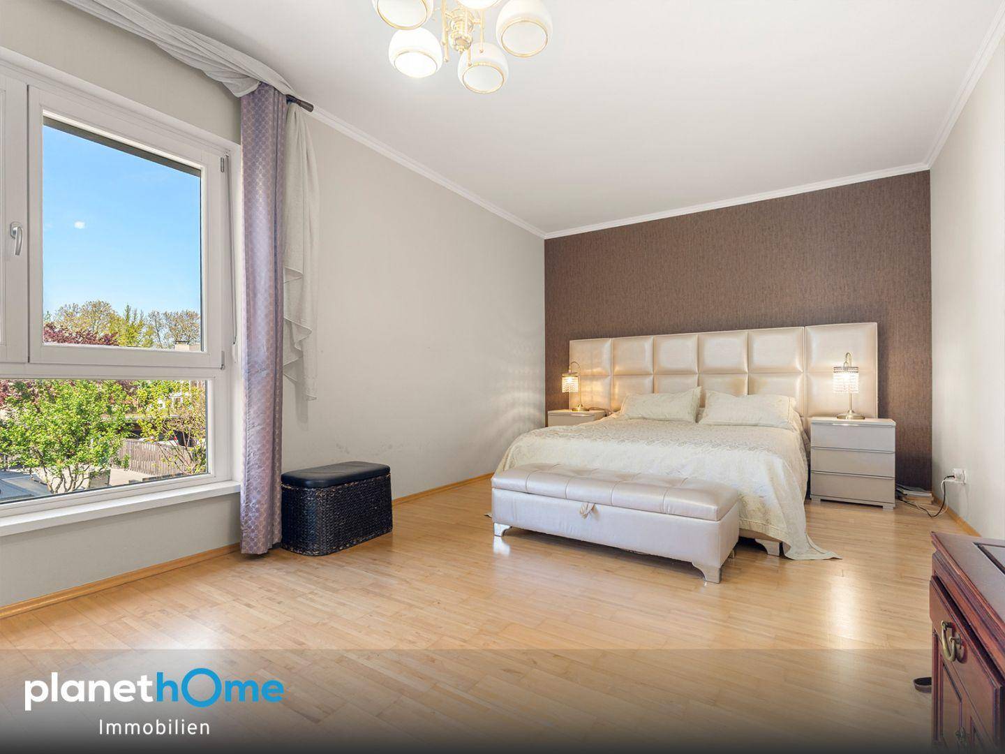 Geräumiges Schlafzimmer mit Holzboden, großem Fenster und einem modernen Doppelbett mit gepolstertem Kopfteil.