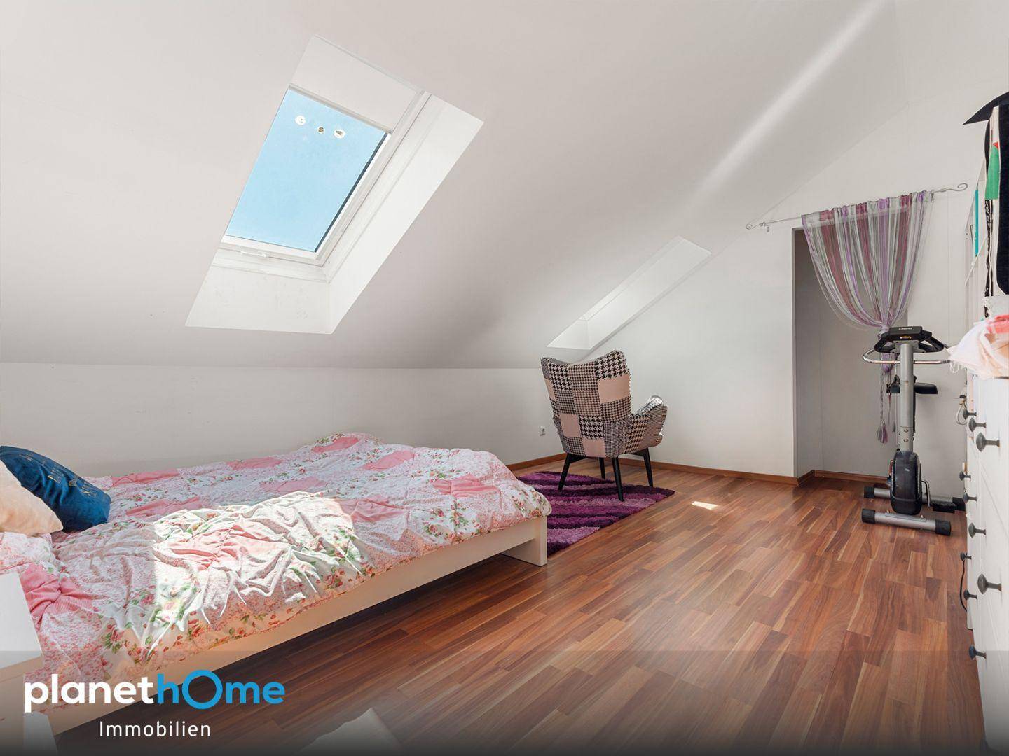Helles Dachgeschosszimmer mit Holzboden, einem großen Dachfenster und gemütlicher Einrichtung.