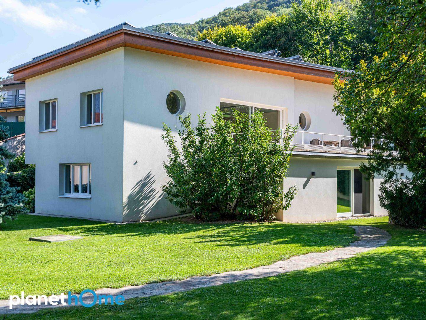 Modernes Einfamilienhaus mit gepflegtem Garten, Rasenfläche und Bergblick im Hintergrund.