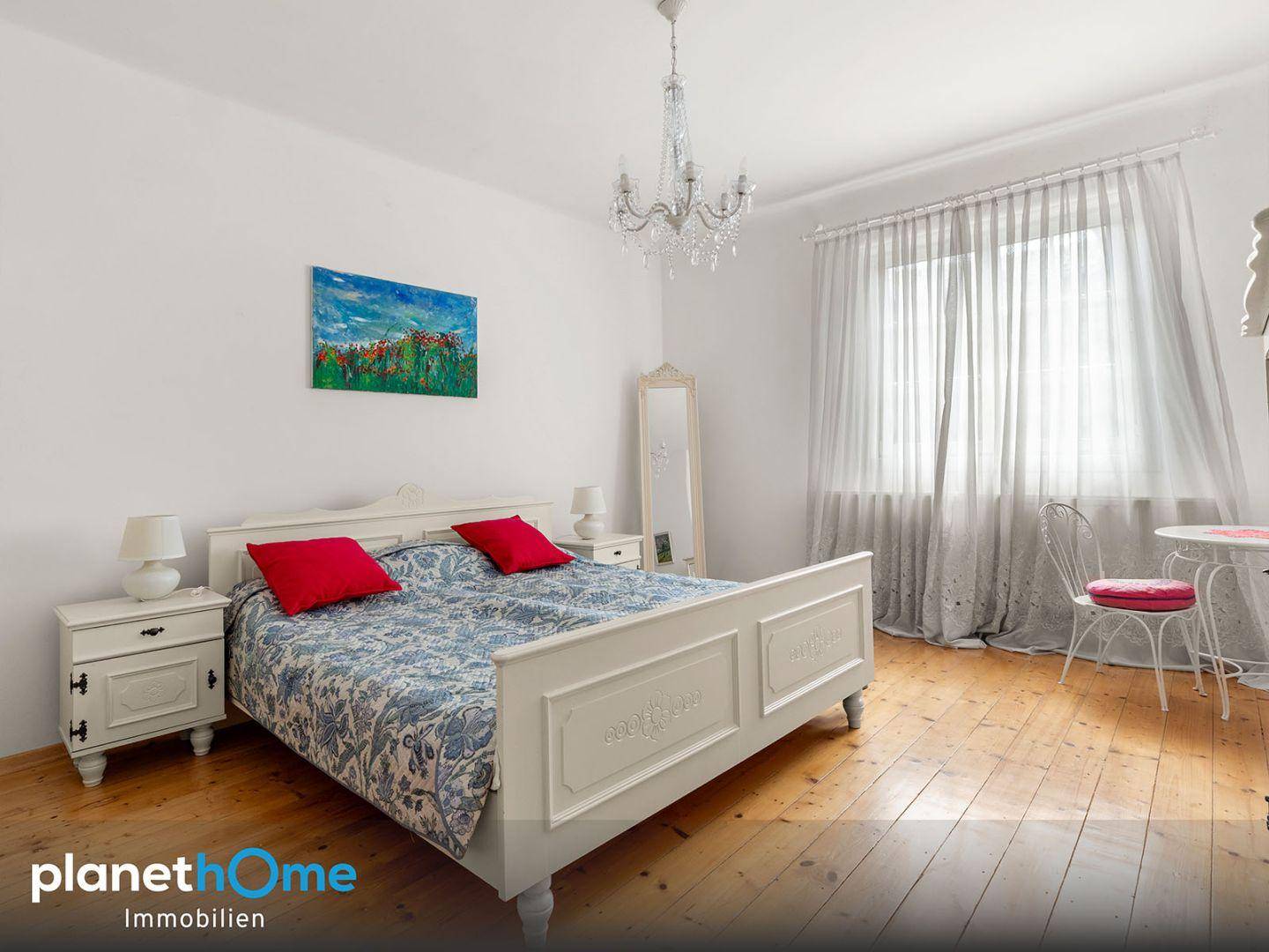 Helles Schlafzimmer mit weißem Bett, Holzboden und Kronleuchter.