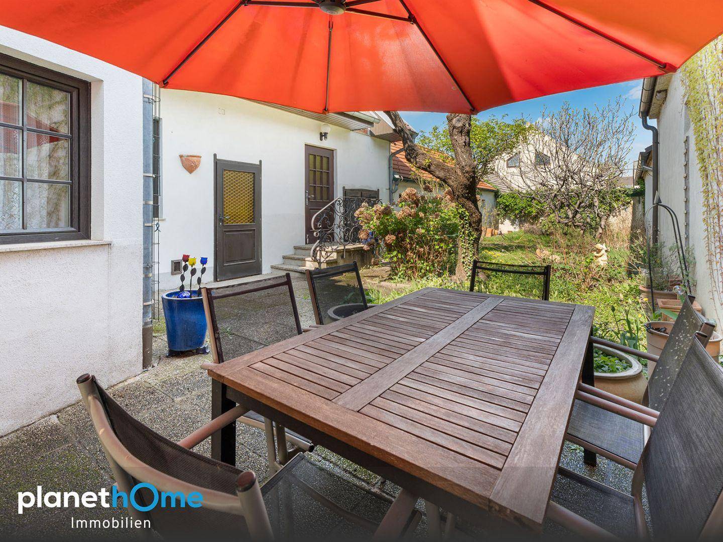 Gemütliche Terrasse mit Holztisch, Stühlen und großem Sonnenschirm im Garten.